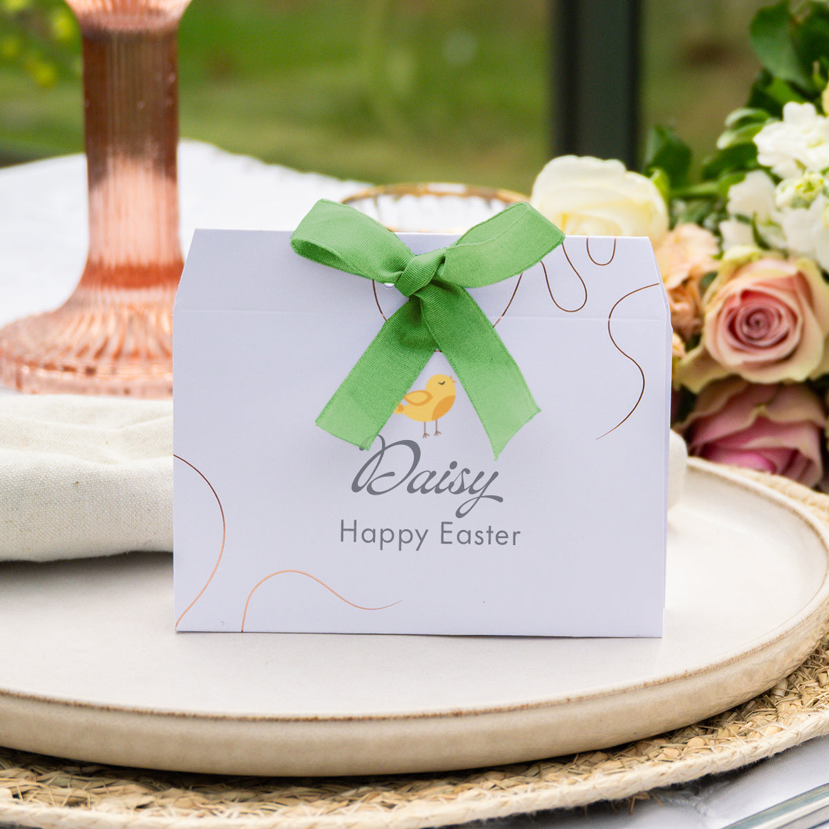 A personalised Easter favour box with a  bright green ribbon bow, and elegant rose-gold line accents. The front of the box is printed with the name 'Daisy' and the phrase 'Something sweet for your Easter Sunday'.