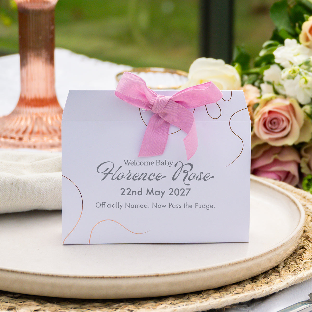 A personalised baby naming favour box with a pink ribbon bow, printed with 'Welcome Florence Rose 22nd May 2027 Officially Named. Now Pass the Fudge.