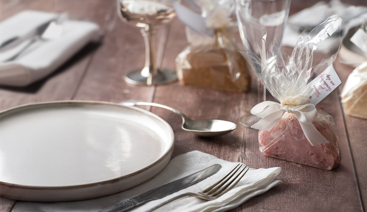 Wedding table setting with handmade fudge favour twist wrapped in clear eco-friendly packaging and tied with a cream ribbon, placed beside a plate and cutlery.